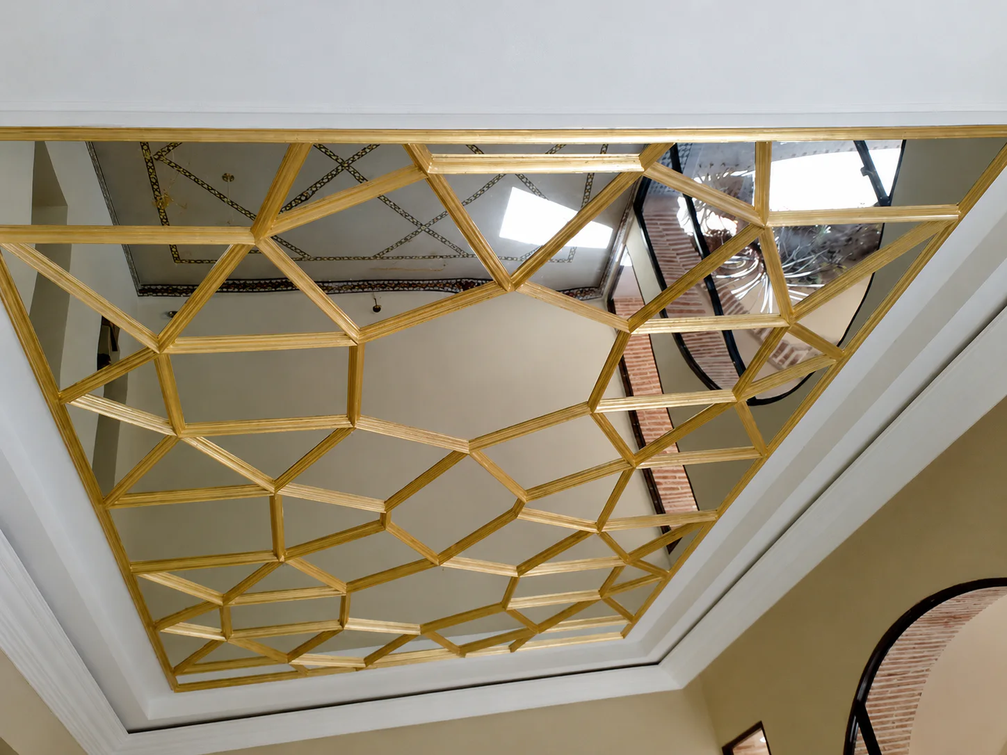Plafond à motif géométrique doré dans un encadrement blanc.