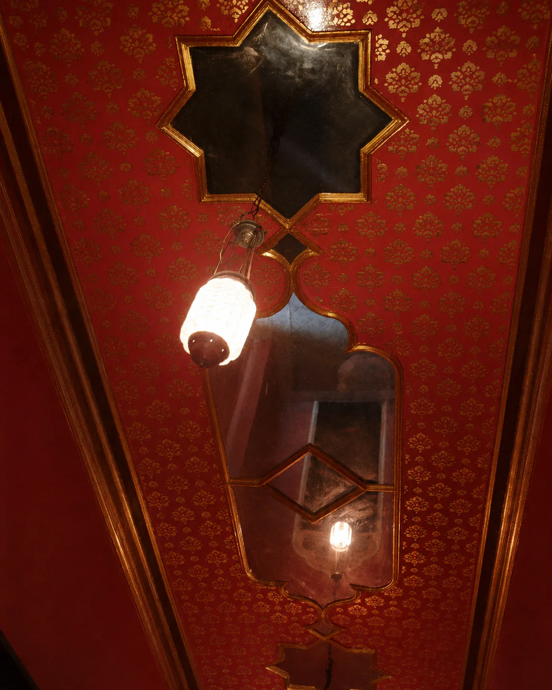 Plafond rouge décoré de miroirs et de cadres dorés.